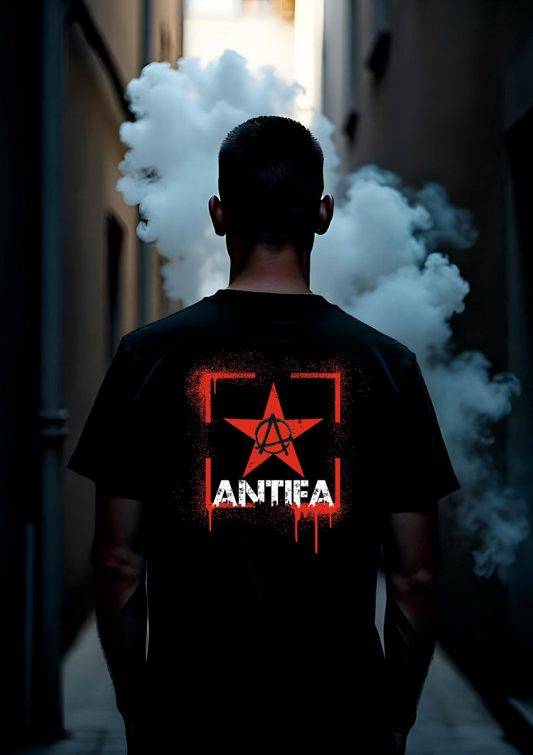 Alt-Text-Vorschlag: Person steht in einem nebligen, engen Durchgang und trägt ein schwarzes T-Shirt mit rotem Stern und Anarcho-Symbol sowie dem Schriftzug „ANTIFA“. Die Szene wirkt rebellisch und geheimnisvoll.