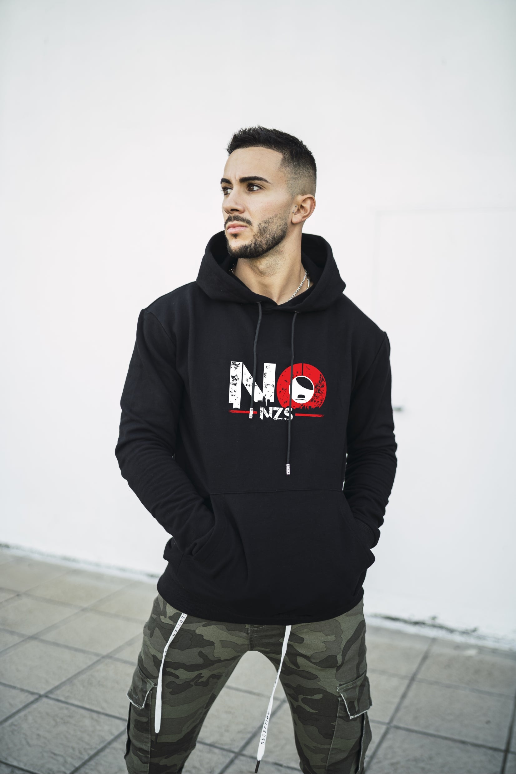 Person trägt schwarzen Hoodie mit weiß-rotem „NO FNZS“-Print auf der Brust – das „O“ ist als roter Kreis mit weißem Symbol gestaltet. Der Look kombiniert klare antifaschistische Botschaft mit urbanem Stil.