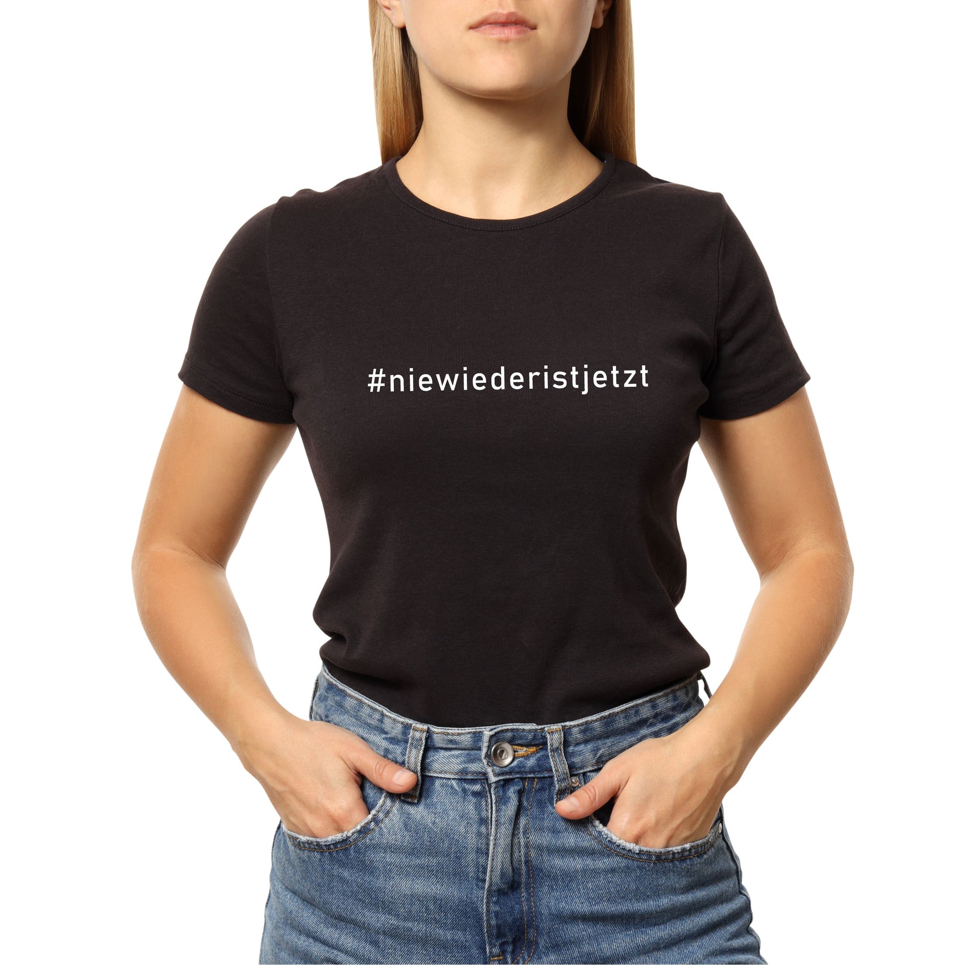 Frau trägt ein schwarzes T-Shirt mit weißem Print „Nie wieder ist jetzt“ auf der Brust; aufgenommen vor hellem Hintergrund. Das Shirt besteht aus Bio-Baumwolle und besitzt einen klassischen Rundhalsausschnitt. Der Schriftzug ist hochwertig im Siebdruckverfahren aufgebracht und symbolisiert eine klare antifaschistische Haltung.
