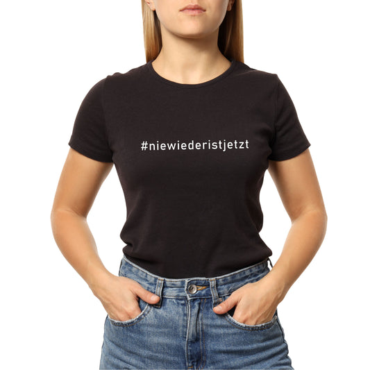 Frau trägt ein schwarzes T-Shirt mit weißem Print „Nie wieder ist jetzt“ auf der Brust; aufgenommen vor hellem Hintergrund. Das Shirt besteht aus Bio-Baumwolle und besitzt einen klassischen Rundhalsausschnitt. Der Schriftzug ist hochwertig im Siebdruckverfahren aufgebracht und symbolisiert eine klare antifaschistische Haltung.
