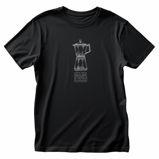 Mokkakanne auf schwarzem T-Shirt. Darunter steht in deutscher Sprache das Zitat: ‚Frieden beginnt, wenn wir lernen, einander zuzuhören – und manchmal ist der erste Schritt eine gemeinsame Tasse Kaffee.