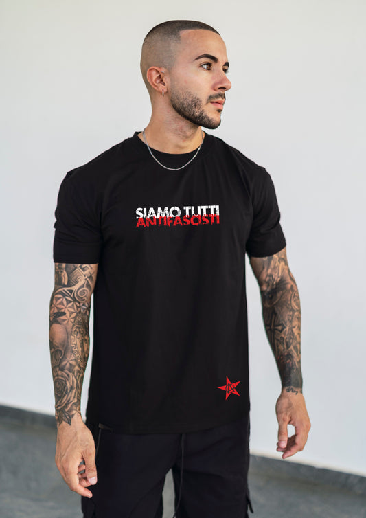 Mann trägt chwarzes Jack & Jones Bio-Baumwoll T-Shirt mit dem roten und weißen Frontprint „Siamo tutti antifascisti“, fotografiert flach von vorne, Statement-Design für Unisex-Mode.